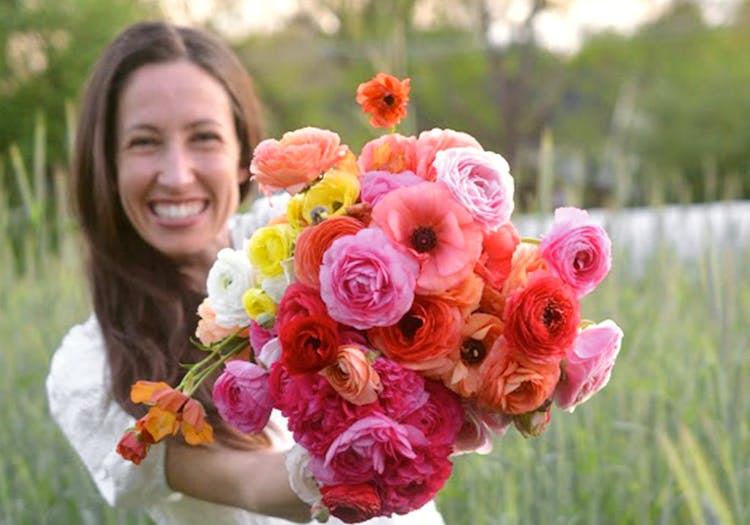 The owner of Eden Roots Flower Farm, holding a bright orange, red, yellow and white bouquet in her field